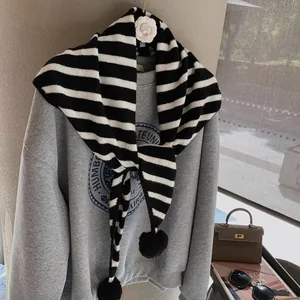 Cute black and white striped knitted scarf with pom-pom details and warm autumn texture