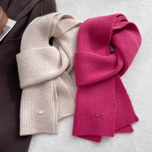 Detail of soft wool knit scarves in beige and rose red with ribbed texture and oval logo