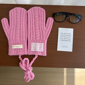 Flat lay of pink cable knit mittens with a neck strap on dark wood texture background