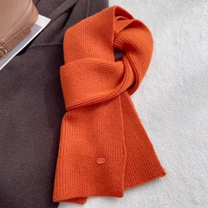 Detail of bright orange wool knit scarf texture and small oval metal brand tag