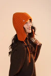 Dettaglio cappello in maglia arancione con stemma in metallo e lacci intrecciati