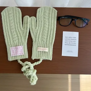 Detailed knit texture of light green winter mittens with a thick hanging rope