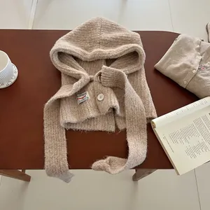Close-up of oatmeal knit balaclava hood with button closure and logo tag on wood desk