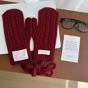 Close-up of dark red cable knit mittens with a neck strap and decorative fabric tags