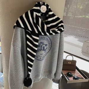 Close-up of black and white striped knit scarf with decorative pom-poms on grey sweatshirt