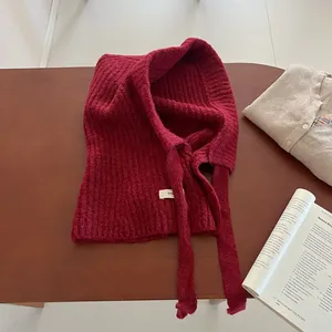 Détail d'une cagoule en maille bordeaux avec étiquette posée sur une table en bois