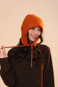 Dettaglio del cappello in maglia arancione vivace con logo in metallo e paraorecchie invernali