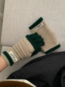 Detail of color-block knit gloves in pumpkin orange and green with woven wrist label