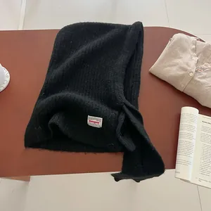 Detail of black ribbed knit balaclava hat featuring a woven brand tag on soft fabric
