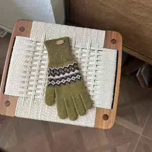Detail von grünen Fair-Isle-Strickhandschuhen mit nordischen Mustern und Lederetikett