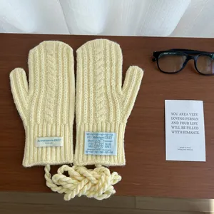 Detail of light yellow cable-knit mittens with lanyard on a cozy wooden desk
