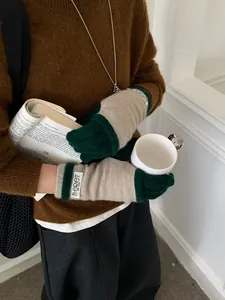 Detail of knit gloves in oatmeal and dark green showing the ribbed cuffs and soft texture