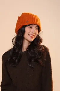 Dettaglio del cappello in maglia arancione con paraorecchie e bottone metallico