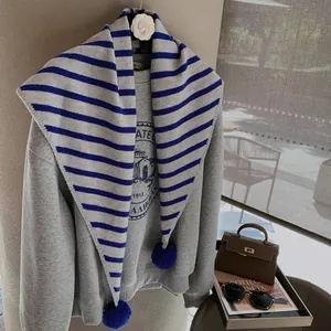 Detail of grey and blue striped knitted scarf with fuzzy pom-poms for autumn outfits