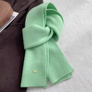 Close-up of mint green wool scarf featuring vertical rib-knit and a golden metal logo tag
