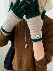 Close-up of contrast knit gloves in green and camel with m.eret label detail
