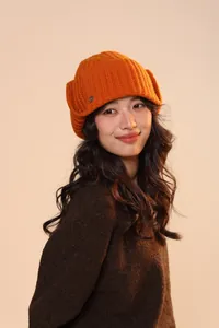 Dettaglio del cappello invernale arancione con paraorecchie e logo sul modello