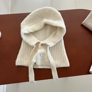 Détail d'une cagoule écrue montrant la maille épaisse côtelée et la fermeture boutonnée
