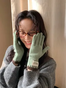 Close-up of light green knitted gloves with contrast cuffs and woven label detail