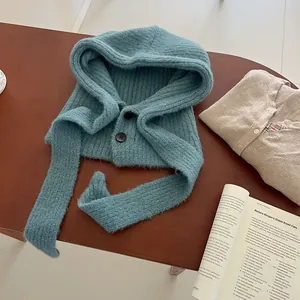 Detail view of teal rib-knit balaclava hat with double black buttons on wood desk