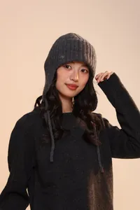 Dettaglio del cappello da aviatore grigio scuro con logo metallico e maglia spessa