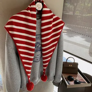 Detail of red and white striped knit triangle scarf with soft decorative plush pom-poms