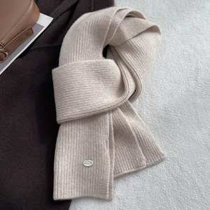 Nahaufnahme von Strickschal aus Wolle in Haferflocken-Farbe mit silbernem Logo-Schildchen