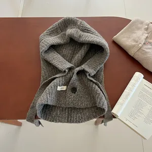 Cagoule écharpe en grosse maille grise avec boutons noirs sur fond de table en bois