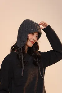 Dettaglio del cappello aviatore in maglia grigio scuro con paraorecchie e logo in metallo