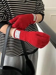 Detail of red ribbed knit gloves featuring contrast beige cuffs and a textile brand label
