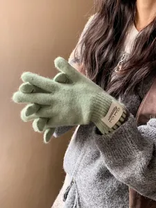 Close-up of soft light green knit gloves featuring a Silent Wind woven brand label