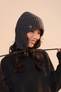 Dettaglio del cappello in maglia grigio scuro con paraorecchie e logo in metallo