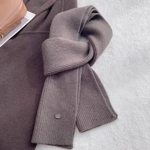 Detail view of the ribbed knit wool texture and metal brand tag on the brown scarf