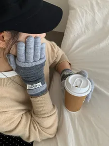 Detail of grey knitted touchscreen gloves with brand label holding a coffee cup