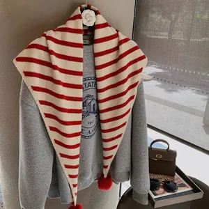 Detail of red and white striped knit scarf with fluffy pom-poms on soft fabric