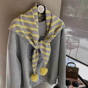 Detail of grey striped knit scarf with bright yellow pom-poms and retro graphic sweatshirt