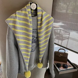 Detail of grey sweatshirt with a striped yellow and grey knit shawl and soft pom-poms
