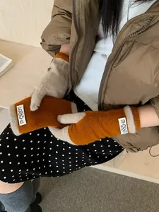 Detail view of pumpkin orange knit gloves with beige trim and branded fabric tag
