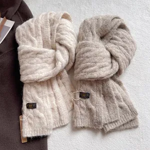 Thick cable knit wool scarves in cream and light brown on a textured white background