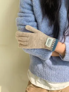 Detail of camel knitted gloves featuring blue ribbed cuffs and a white textile label