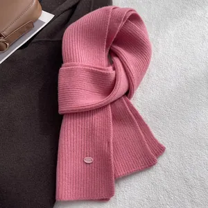 Detailaufnahme des rosa Wollstrickschals mit Rippenmuster und Markenetikett auf braunem Mantel