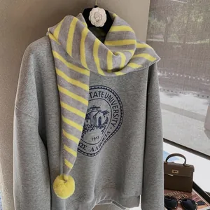 Detail of knit striped scarf with yellow pompom over a grey college sweatshirt