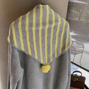 Detail of yellow and grey striped knit shawl featuring a soft decorative pom-pom