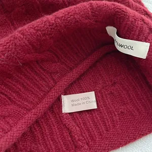 Detail der 100% Wolle Kennzeichnung und der groben Zopfstrickstruktur dieser Mütze
