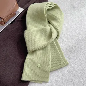 Macro detail of ribbed sage green wool scarf with minimalist oval brand patch