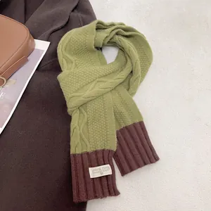 Detail of green and brown knit scarf showing cable texture and minimalist fabric label