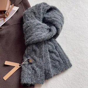 Detailed texture of dark grey thick knit wool scarf with cable knit pattern and brand tag