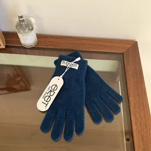Detailed view of dark blue knitted gloves with authentic brand labels on a glass table