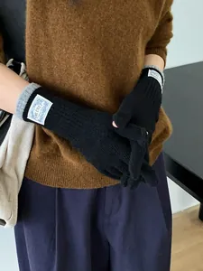 Close-up of black knit gloves with grey cuffs and white label on a model's hand