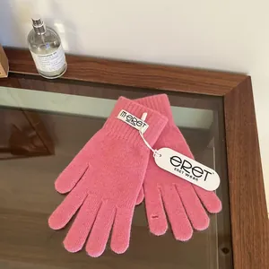 Close-up of pink knit gloves with detailed texture and brand tag on a glass surface